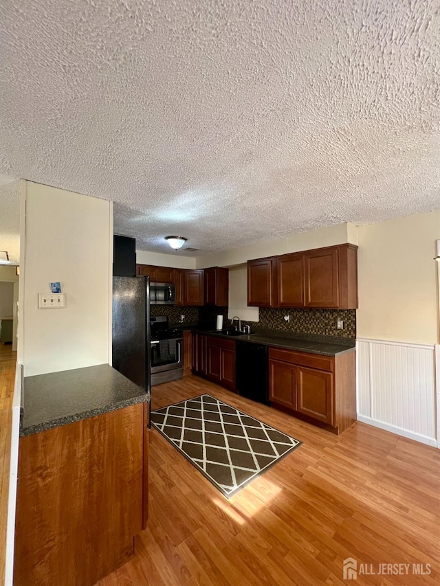 kitchen featuring black appliances, dark countertops, light wood-style flooring, a textured ceiling, and a wainscoted wall