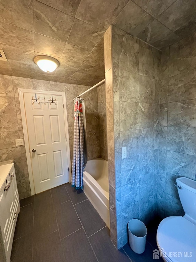 full bath with tile walls, shower / bathtub combination with curtain, vanity, tile patterned floors, and toilet
