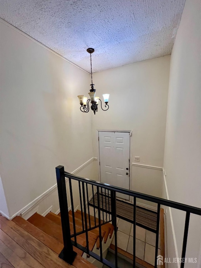 staircase featuring a textured ceiling, a chandelier, baseboards, and wood finished floors