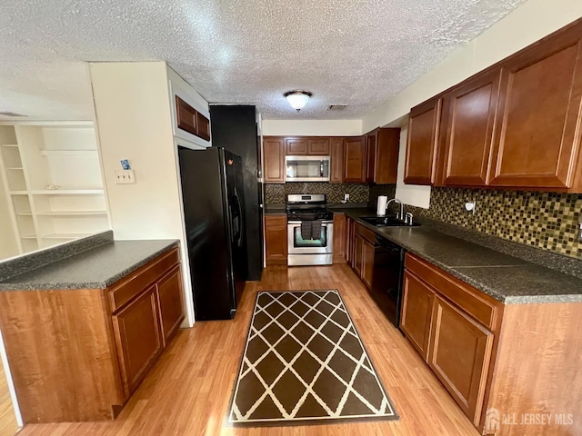 kitchen with black appliances, a sink, dark countertops, light wood-style flooring, and a textured ceiling