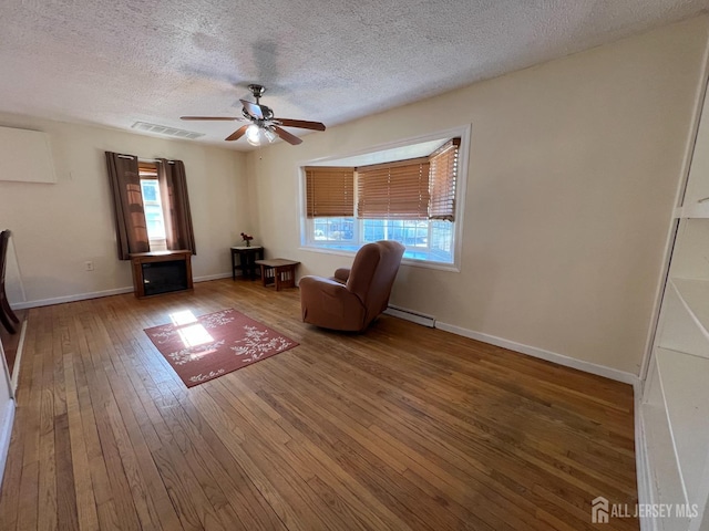 sitting room featuring wood-type flooring, a ceiling fan, a textured ceiling, a baseboard radiator, and baseboards