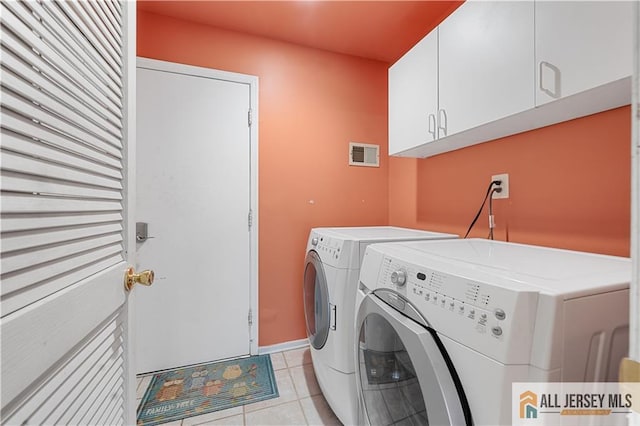 washroom with light tile patterned floors, washing machine and dryer, and cabinets