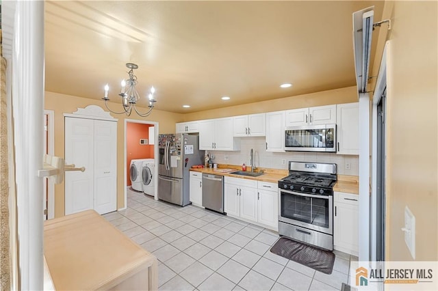 kitchen with appliances with stainless steel finishes, white cabinetry, sink, hanging light fixtures, and washing machine and clothes dryer