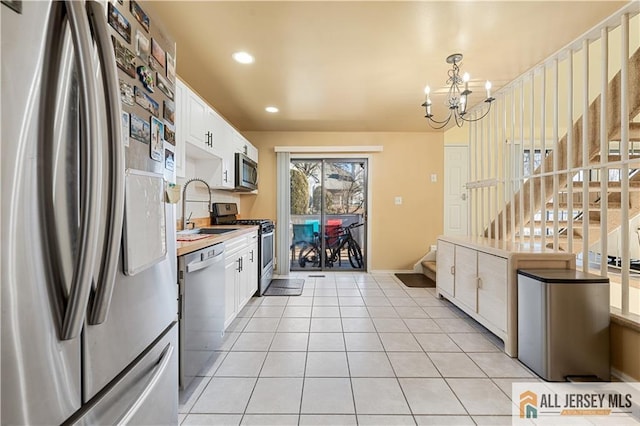 kitchen with appliances with stainless steel finishes, pendant lighting, white cabinetry, sink, and a notable chandelier