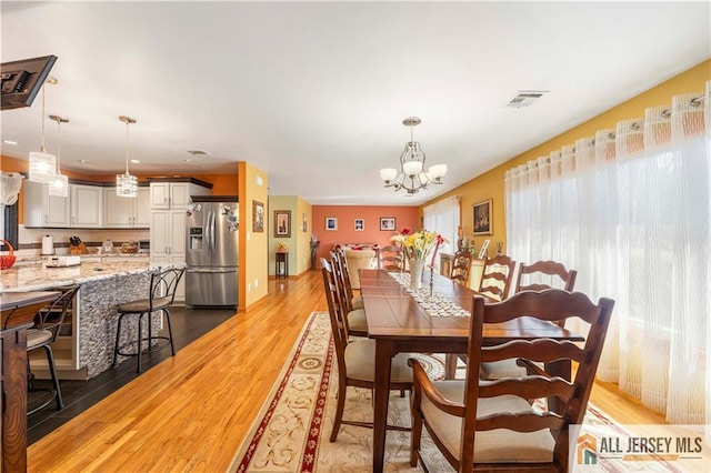 dining area with a chandelier, light wood-type flooring, and visible vents