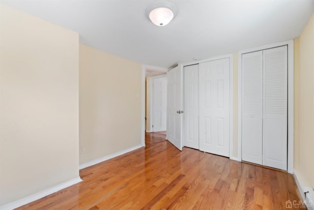 unfurnished bedroom featuring two closets, baseboards, and light wood-type flooring