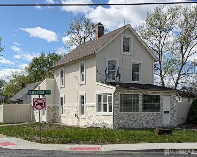 view of side of property featuring stucco siding, fence, a chimney, and stone siding