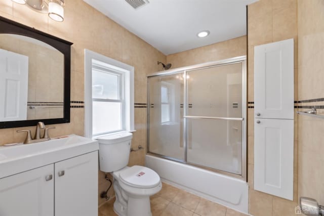 bathroom featuring bath / shower combo with glass door, visible vents, toilet, vanity, and tile patterned flooring