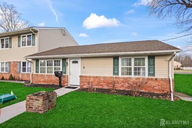 view of front of house with a front yard, brick siding, and roof with shingles