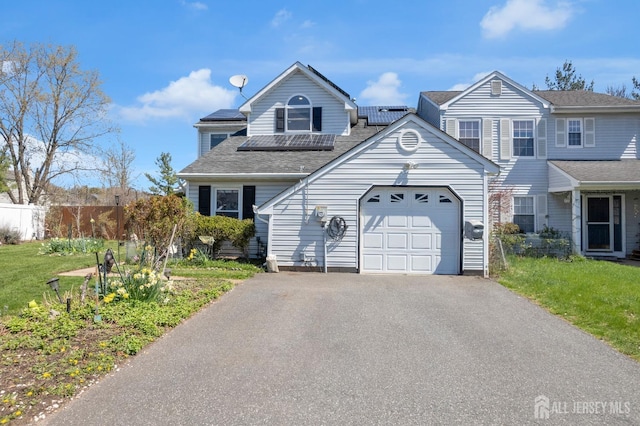 townhome / multi-family property featuring driveway, roof with shingles, a garage, fence, and roof mounted solar panels