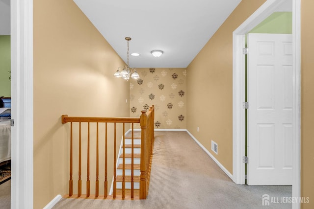 hallway with an inviting chandelier, carpet floors, wallpapered walls, baseboards, and visible vents