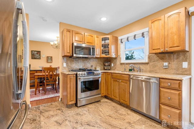 kitchen with decorative backsplash, a sink, light stone counters, glass insert cabinets, and stainless steel appliances
