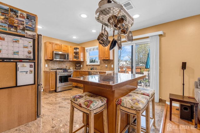 kitchen featuring visible vents, glass insert cabinets, a kitchen bar, appliances with stainless steel finishes, and backsplash