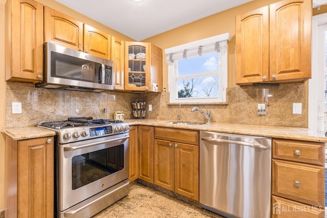 kitchen with decorative backsplash, light stone countertops, glass insert cabinets, a sink, and stainless steel appliances