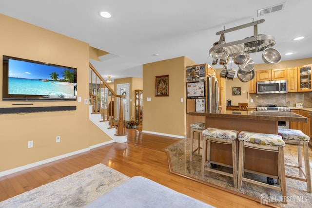 kitchen with a kitchen breakfast bar, visible vents, light wood-type flooring, baseboards, and stainless steel appliances