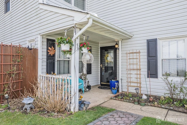 view of exterior entry with a porch and fence