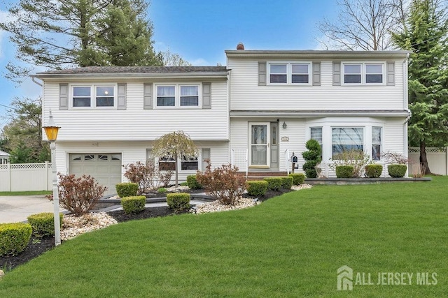 tri-level home with fence, an attached garage, a front lawn, a chimney, and driveway