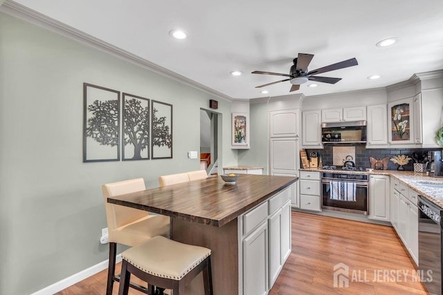 kitchen with a kitchen breakfast bar, wooden counters, appliances with stainless steel finishes, ornamental molding, and recessed lighting