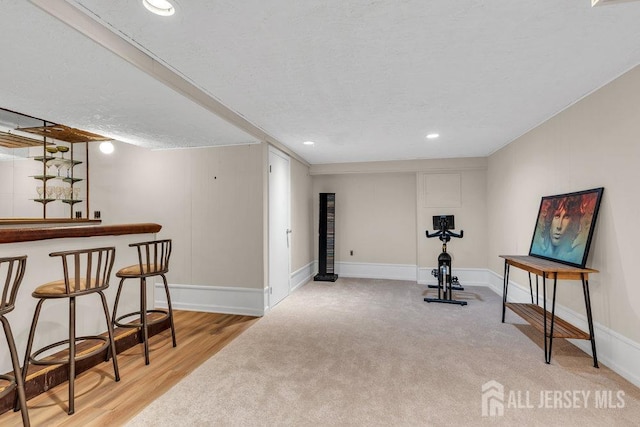 exercise area with a dry bar, a textured ceiling, carpet, baseboards, and wood finished floors