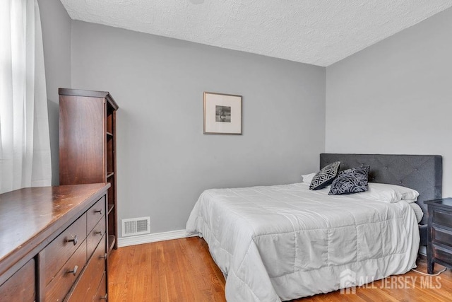 bedroom with visible vents, a textured ceiling, light wood finished floors, and baseboards