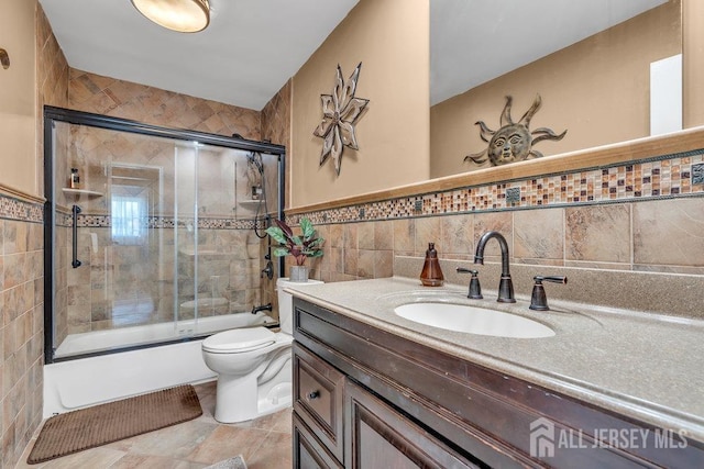 full bathroom featuring tile walls, vanity, toilet, and shower / bath combination with glass door