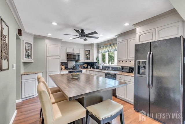 kitchen featuring a sink, black appliances, ornamental molding, and glass insert cabinets
