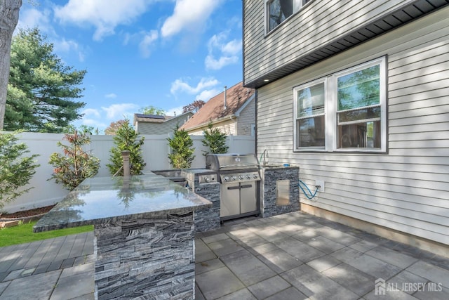view of patio with exterior kitchen, a fenced backyard, grilling area, and a bar