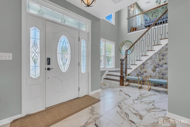 foyer featuring marble tiled floors, baseboards, stairs, and a high ceiling