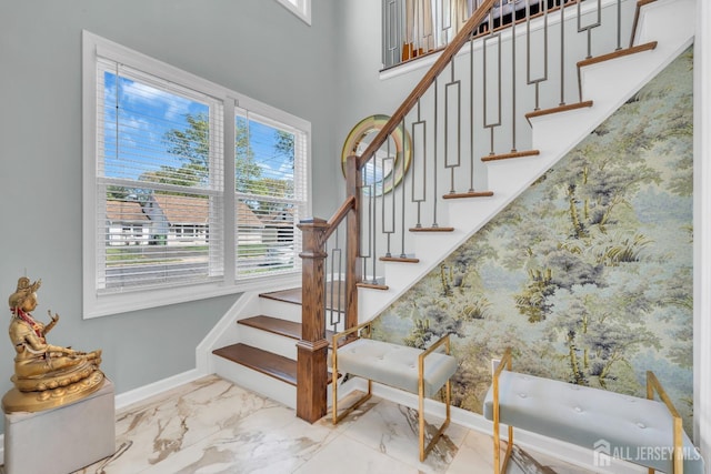 stairs featuring marble look tiles, baseboards, and a high ceiling