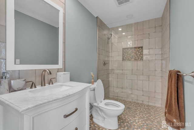 bathroom featuring tiled shower, toilet, vanity, and ornamental molding
