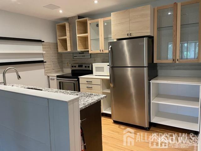 kitchen featuring sink, light wood-type flooring, stainless steel appliances, light stone countertops, and decorative backsplash