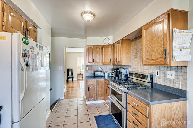 kitchen with decorative backsplash, range with two ovens, white fridge with ice dispenser, and light tile patterned flooring