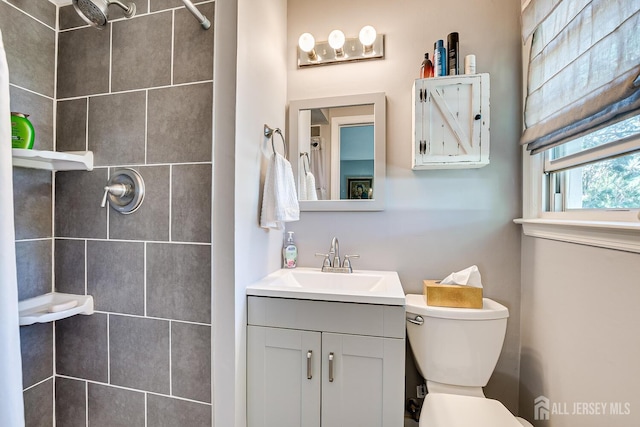 bathroom featuring a tile shower, vanity, and toilet