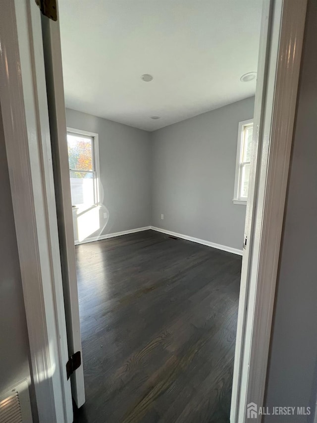 unfurnished room featuring plenty of natural light, baseboards, and dark wood-type flooring