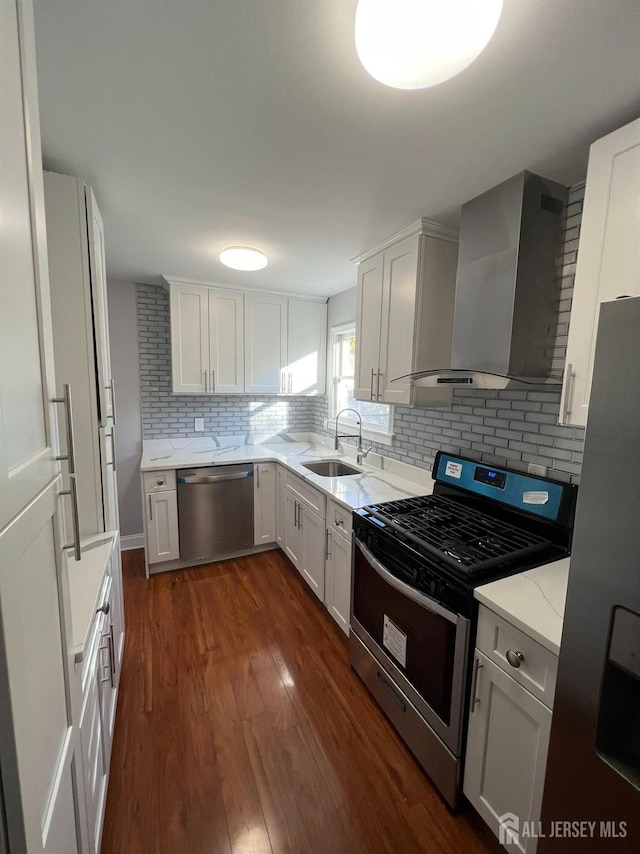 kitchen featuring stainless steel appliances, wall chimney range hood, a sink, dark wood finished floors, and tasteful backsplash