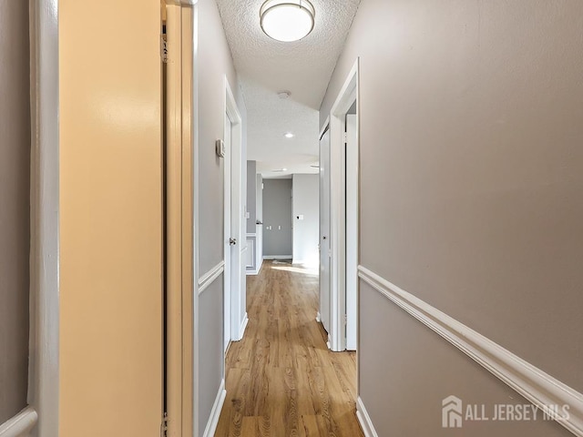 hallway with a textured ceiling and light hardwood / wood-style flooring