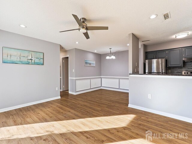 interior space featuring ceiling fan with notable chandelier, hardwood / wood-style floors, stainless steel refrigerator, hanging light fixtures, and a textured ceiling