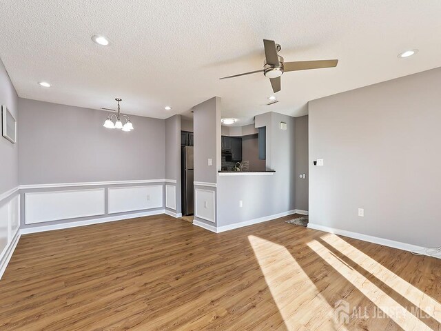 unfurnished living room featuring wood-type flooring, ceiling fan with notable chandelier, and a textured ceiling