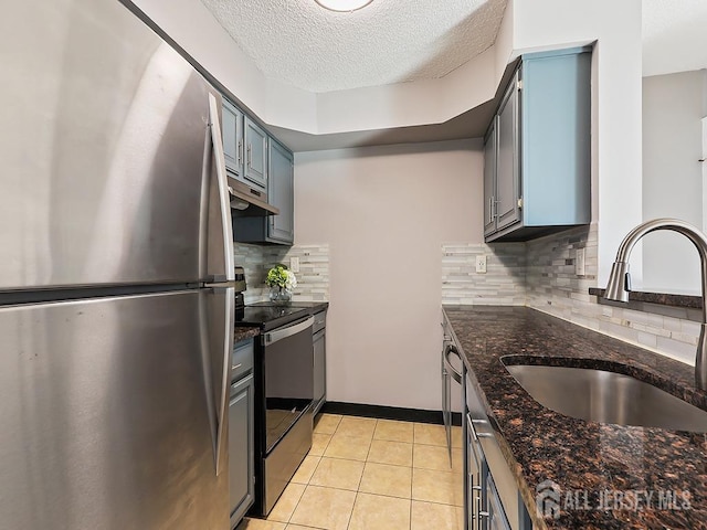 kitchen with appliances with stainless steel finishes, sink, dark stone counters, light tile patterned floors, and a textured ceiling