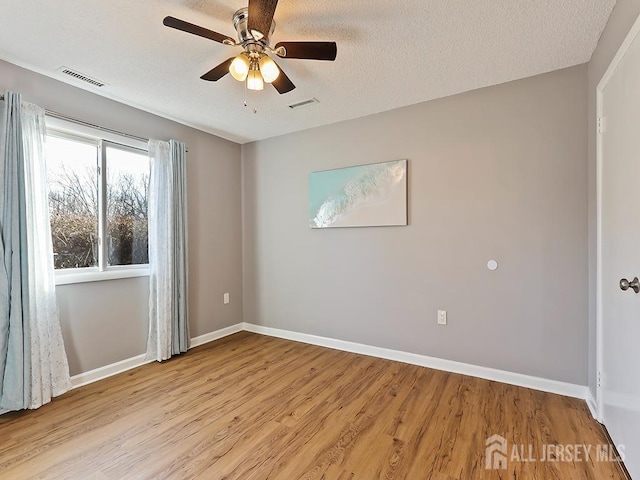 empty room with ceiling fan, light hardwood / wood-style flooring, and a textured ceiling