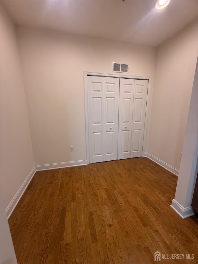 unfurnished bedroom featuring wood finished floors, baseboards, a closet, and recessed lighting