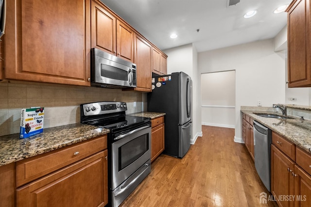kitchen with stainless steel appliances, a sink, brown cabinetry, light wood-type flooring, and recessed lighting