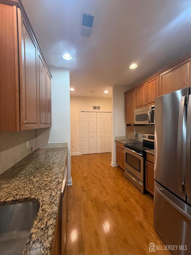 kitchen featuring appliances with stainless steel finishes, light wood-type flooring, brown cabinetry, recessed lighting, and backsplash