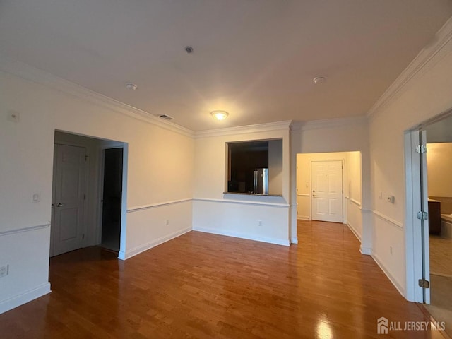 empty room with wood finished floors, crown molding, and baseboards