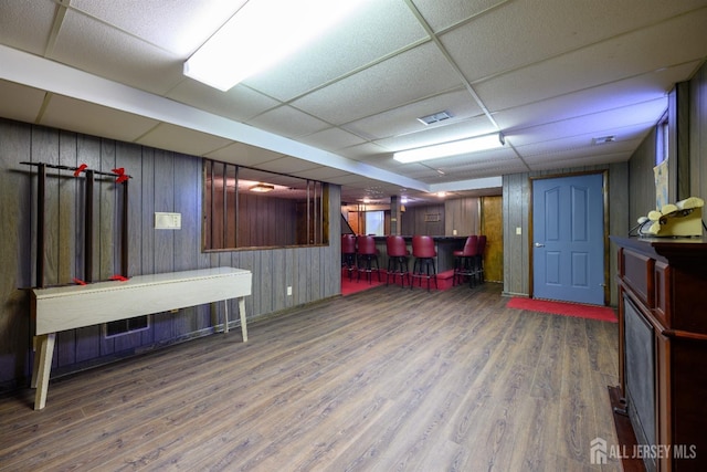 interior space with wood walls, wood-type flooring, a paneled ceiling, and indoor bar