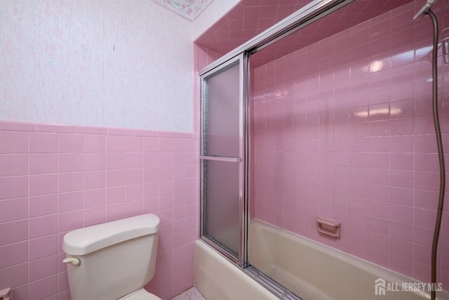 bathroom featuring toilet, combined bath / shower with glass door, and tile walls