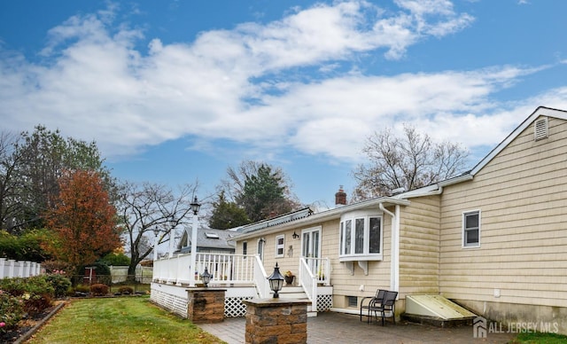 back of property with a deck, a patio area, and a lawn