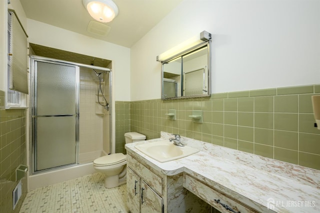 bathroom with toilet, tile walls, a shower with shower door, and vanity