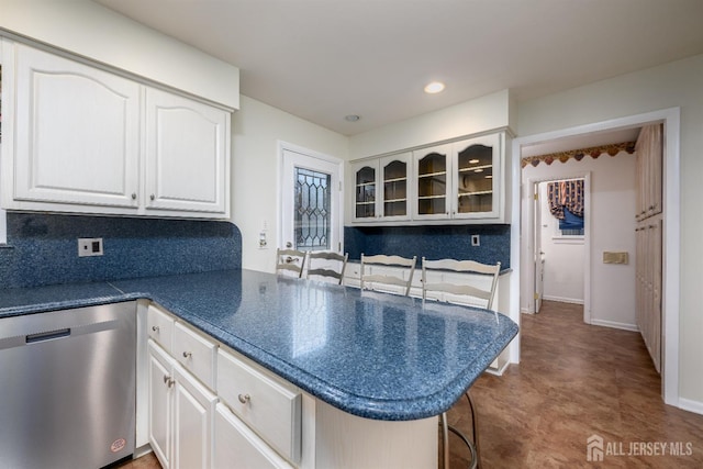 kitchen featuring stainless steel dishwasher, kitchen peninsula, decorative backsplash, white cabinetry, and a kitchen breakfast bar