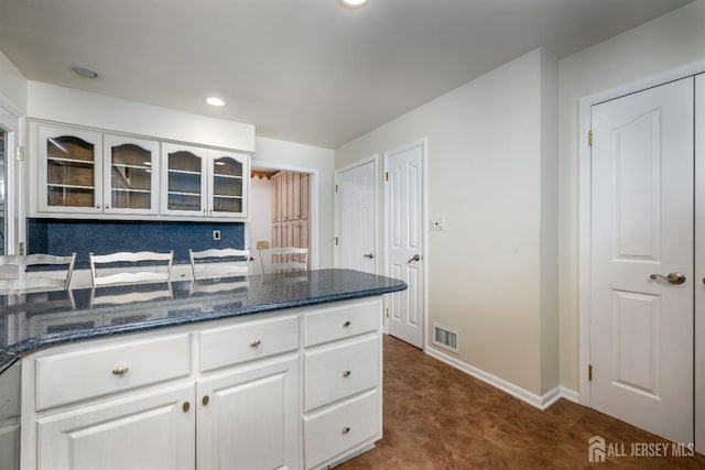 kitchen with white cabinetry, dark carpet, dark stone countertops, and tasteful backsplash